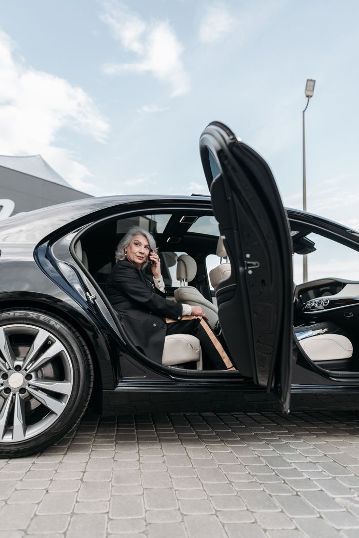 Confident senior woman sitting in a black luxury car, exuding elegance and success.